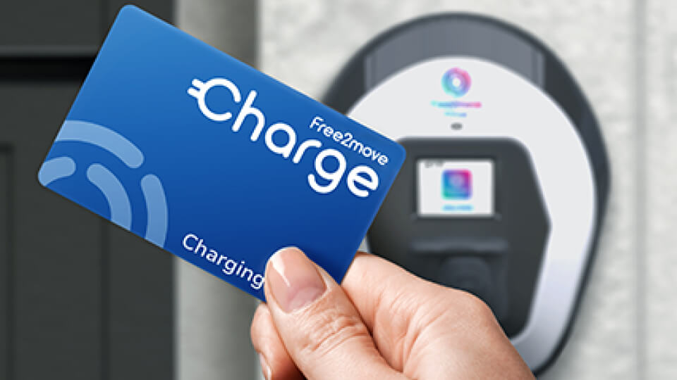 Una mano tiene una carta contactless Free2move Charge vicino a un punto di ricarica per veicoli elettrici